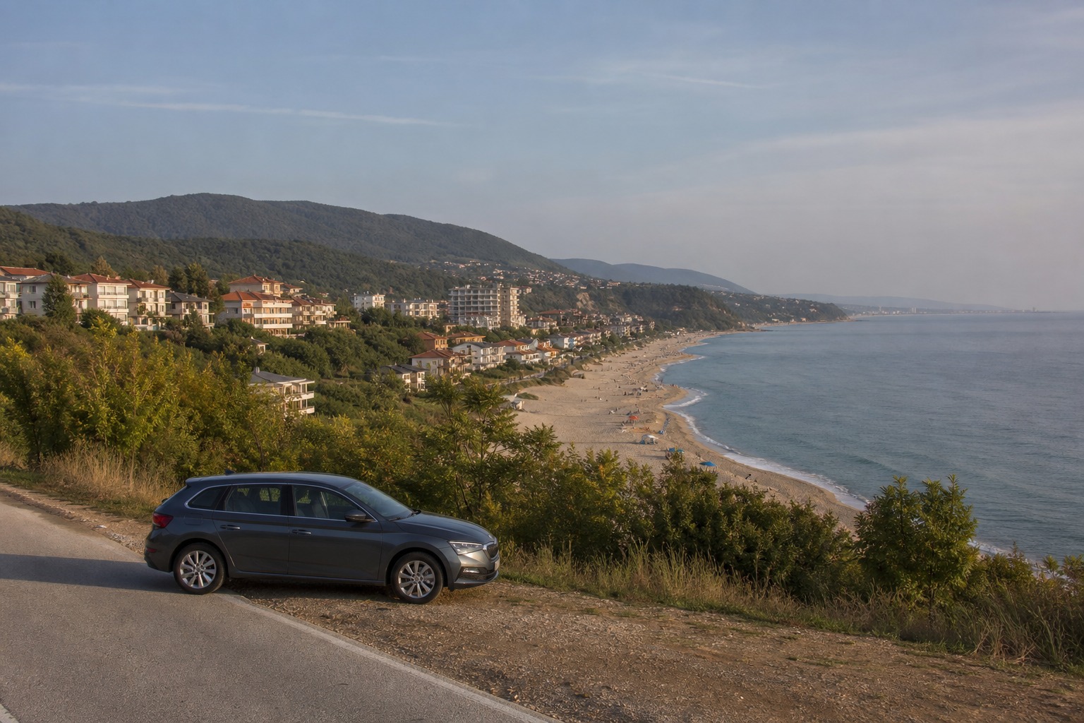 Šedý hatchback na pobřežní silnici s výhledem na pláž a budovy — Pronájem auta v Long Beach Resort